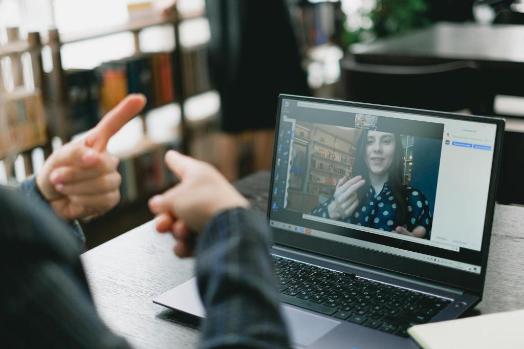 Image of person using sign language to communicate with another person that is shown on their laptop screen.